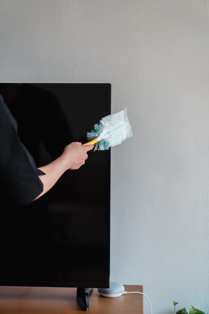 Close-up of a person dusting a TV screen using a cleaning tool indoors.